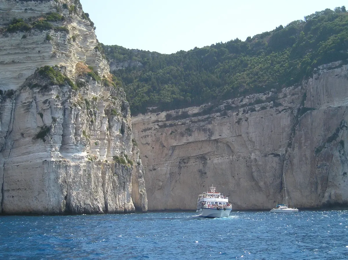A cruise boat below the white cliffs and sea caves on the west coast of Paxos on a Corfu boat tour